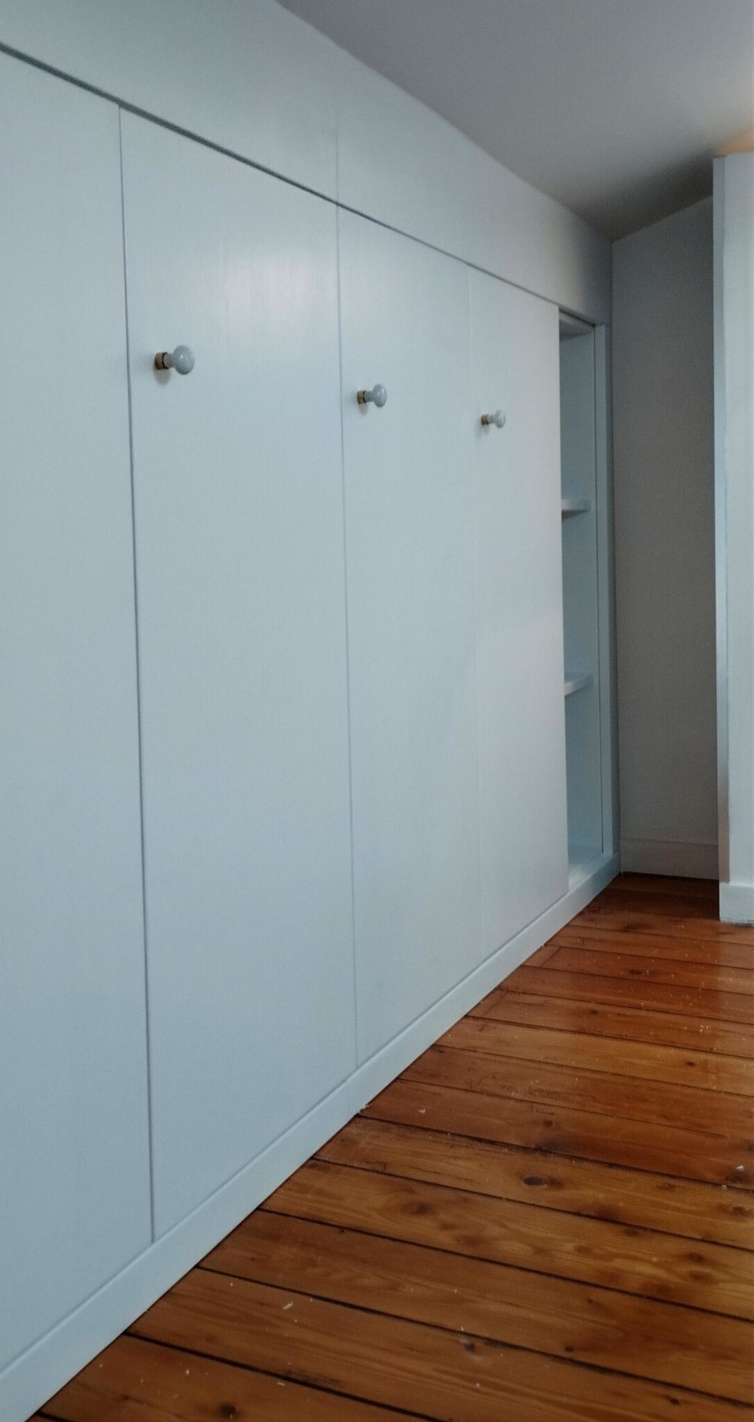 Aménagement de salon sur mesure Dressing sur mesure sous pente avec portes en épicéa laqué blanc et boutons nacrés.