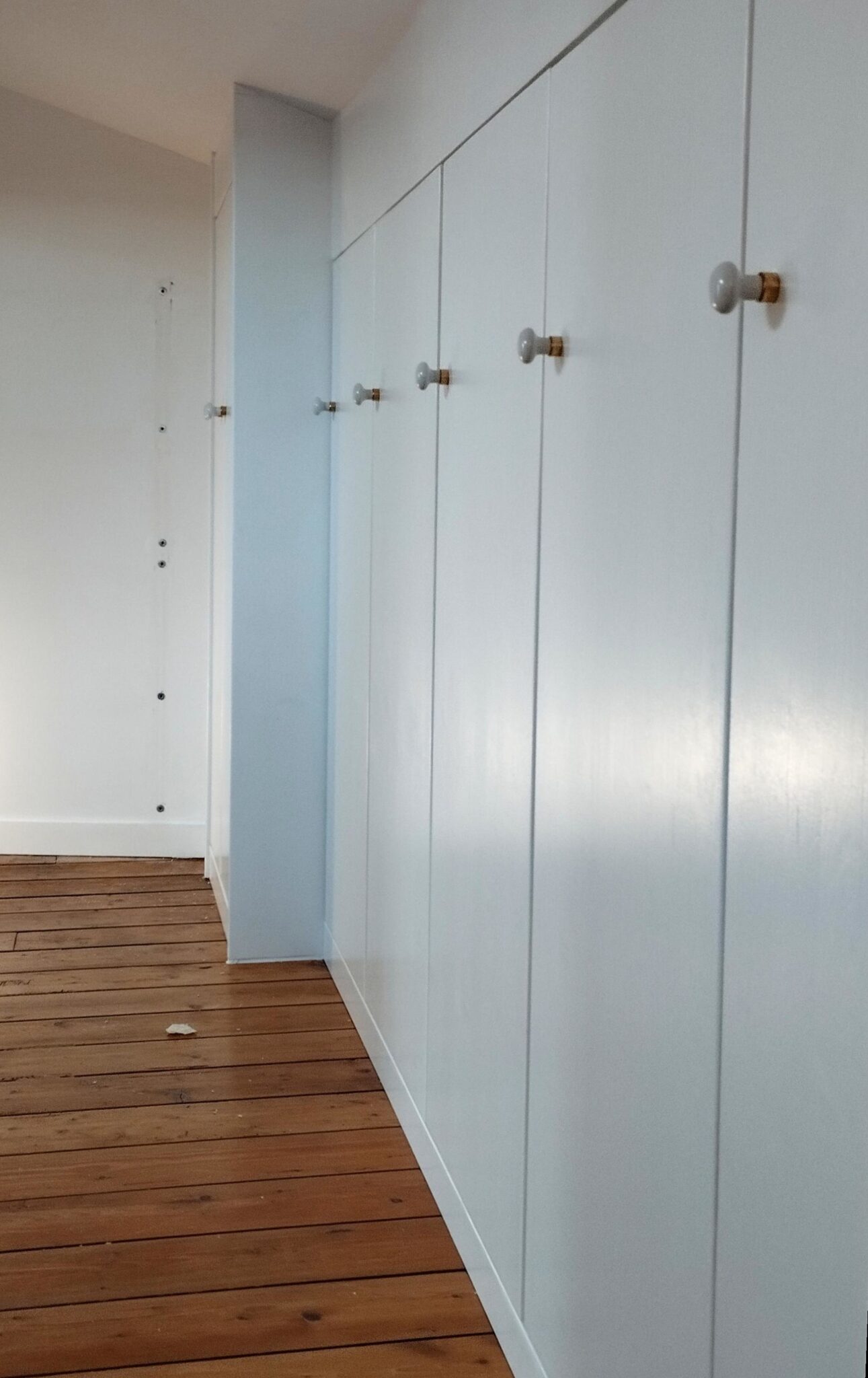 Étagère flottante en MDF laqué Portes en épicéa laqué blanc avec boutons nacrés sur dressing sous pente.